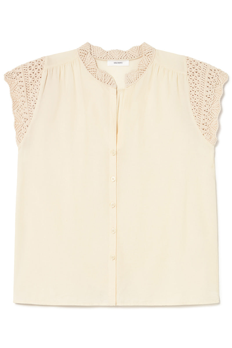 A cream-colored sleeveless blouse with a scalloped lace collar and lace detailing on the shoulders, featuring a button-down front.