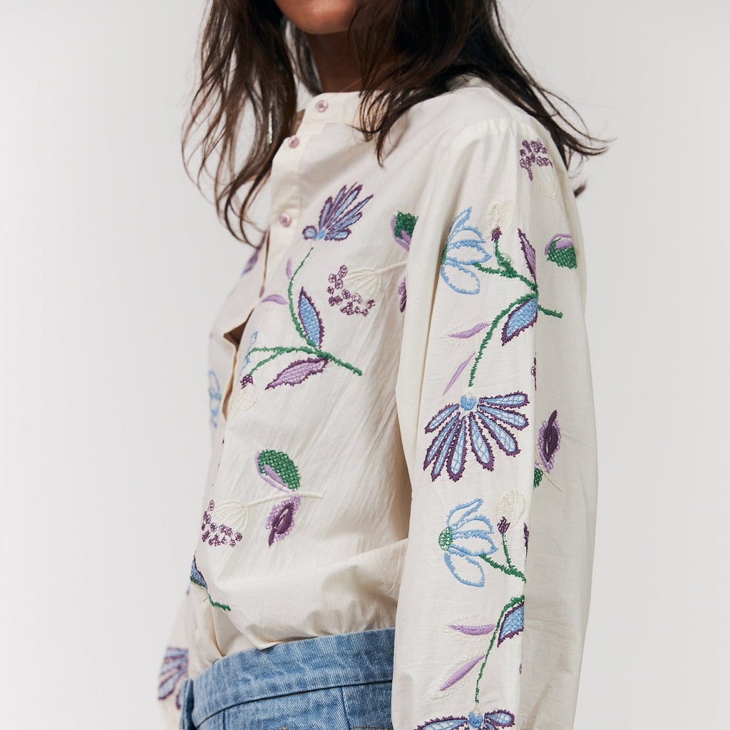 Woman wearing a white blouse with floral embroidery and blue jeans on a white background