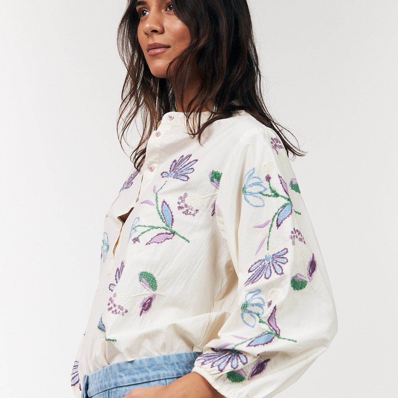 Woman wearing a white blouse with colorful floral embroidery on a plain background