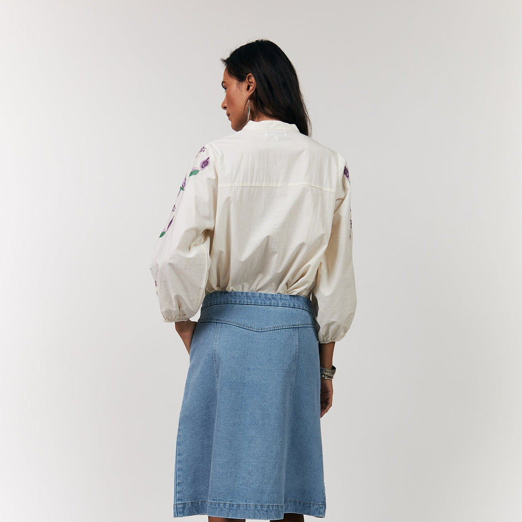 Person wearing a light-colored jacket and blue denim skirt on a white background