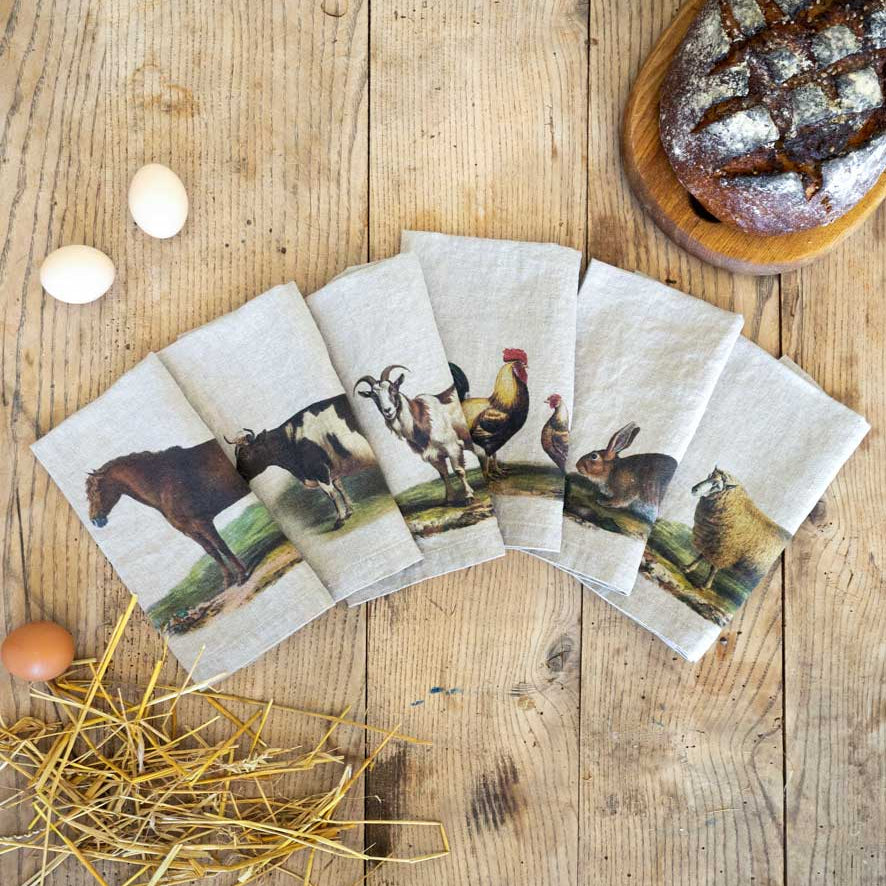 Set of animal-themed napkins on a wooden surface with bread and eggs.