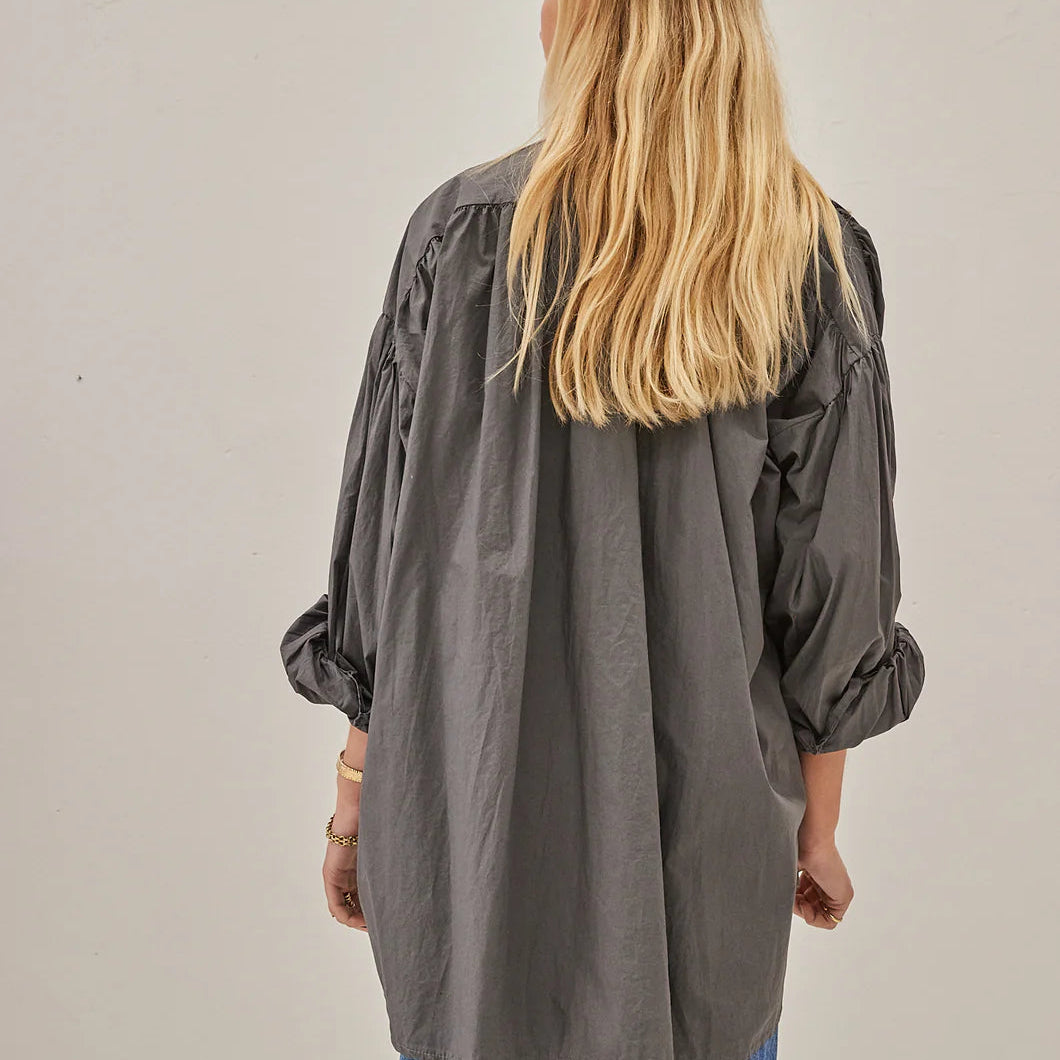 Person wearing a gray oversized shirt and blue jeans against a plain background