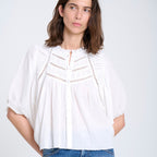 Woman wearing a white blouse and blue jeans against a plain background