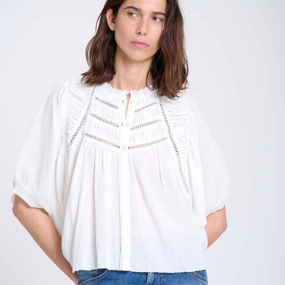 Woman wearing a white blouse and blue jeans against a plain background