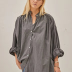 Woman wearing a gray blouse with rolled-up sleeves against a plain background
