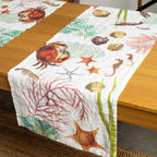 A white table runner with a colorful ocean-themed print featuring starfish, seahorses, crabs, shells, and coral, draped over a wooden dining table.