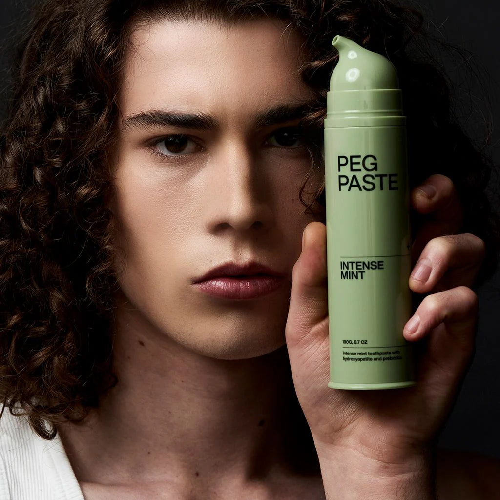 Person holding a green can of 'PEG PASTE Intense Mint' against a dark background