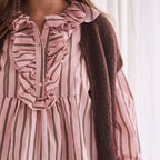 Close-up of a person wearing a pink striped blouse with a brown cardigan.