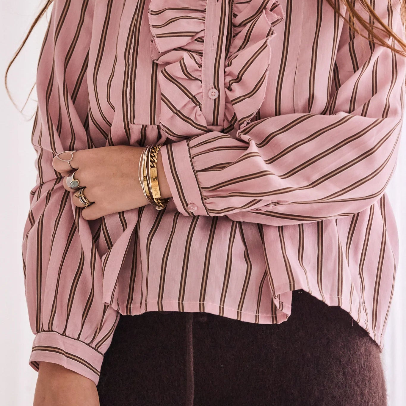 Person wearing a pink and white striped blouse with ruffled details.