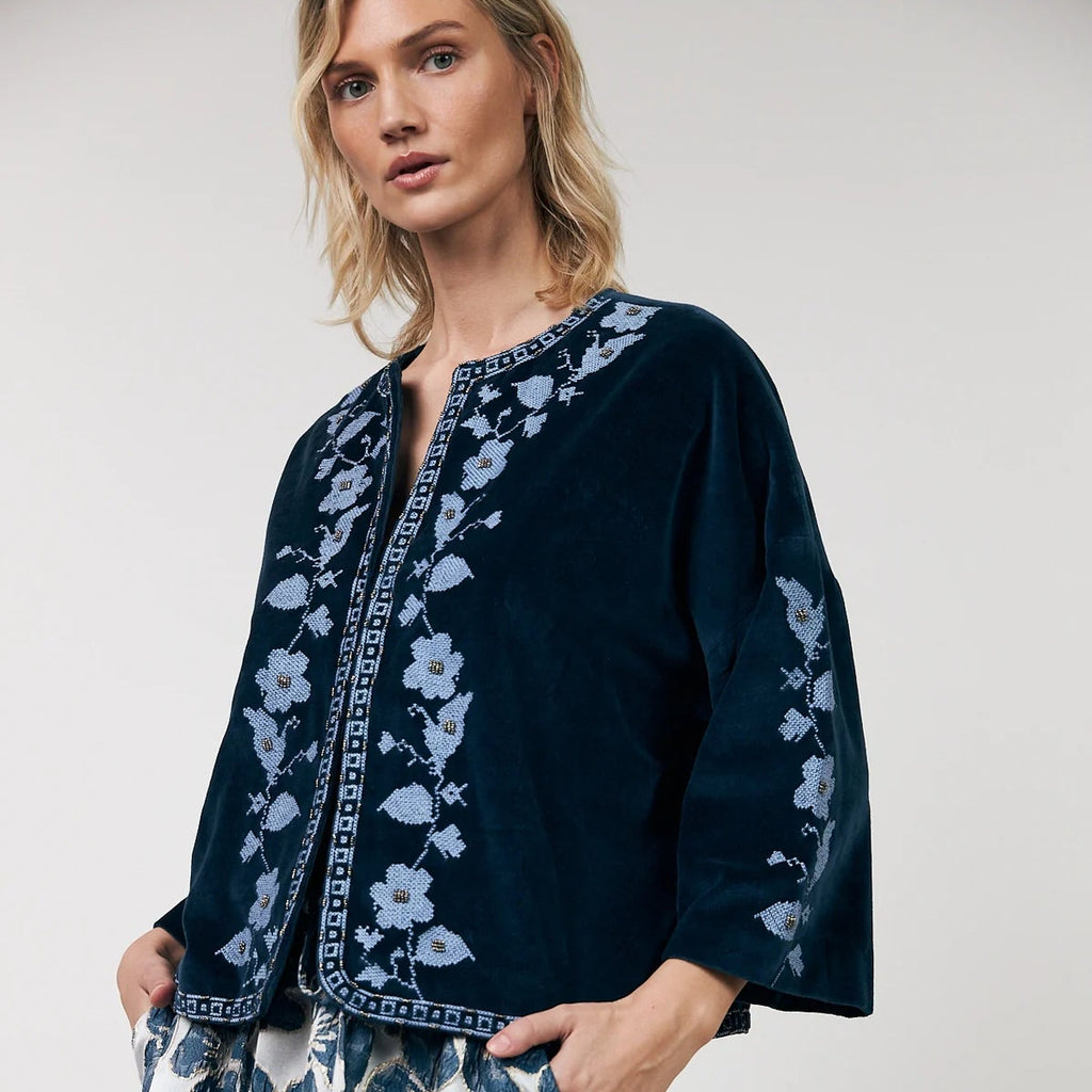 Woman wearing a navy embroidered top and floral skirt on a white background