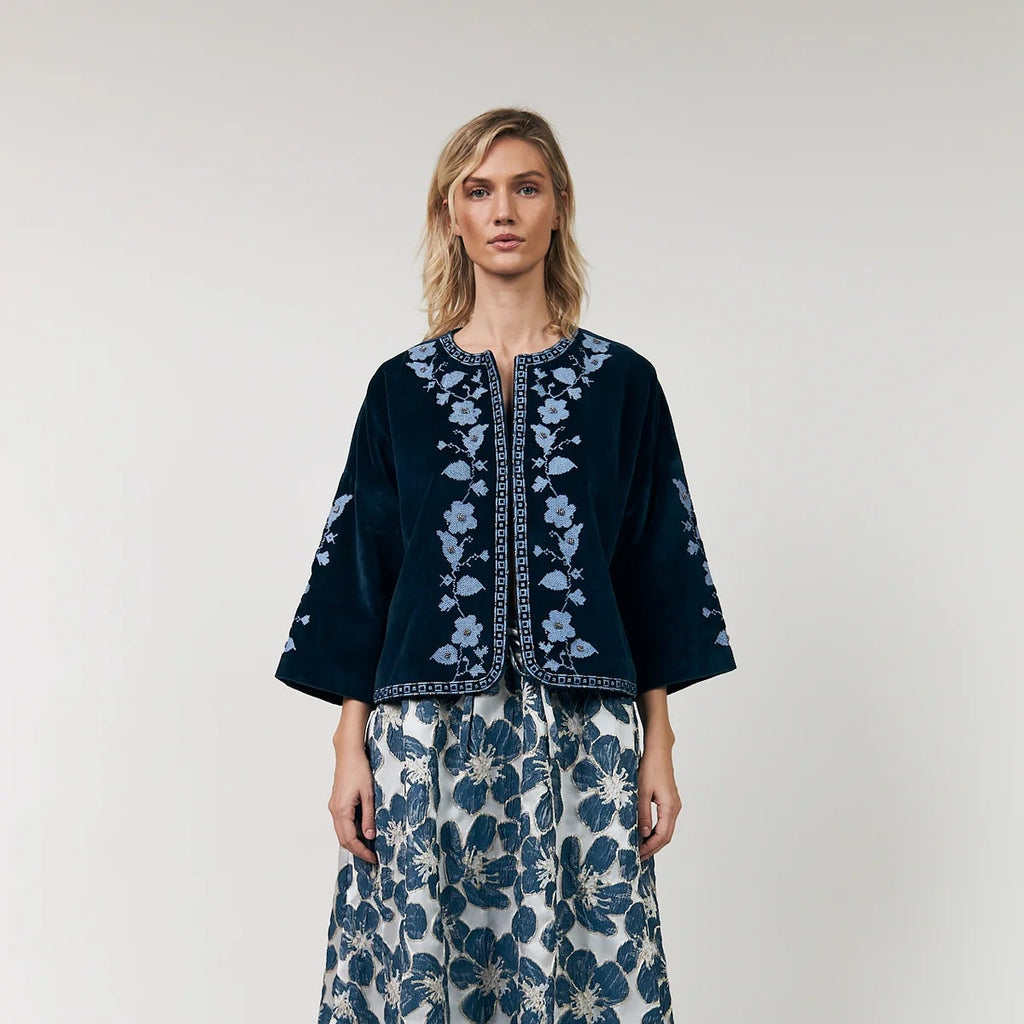 Woman wearing a dark blue embroidered top and floral skirt on a white background