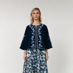 Woman wearing a dark blue embroidered top and floral skirt on a white background