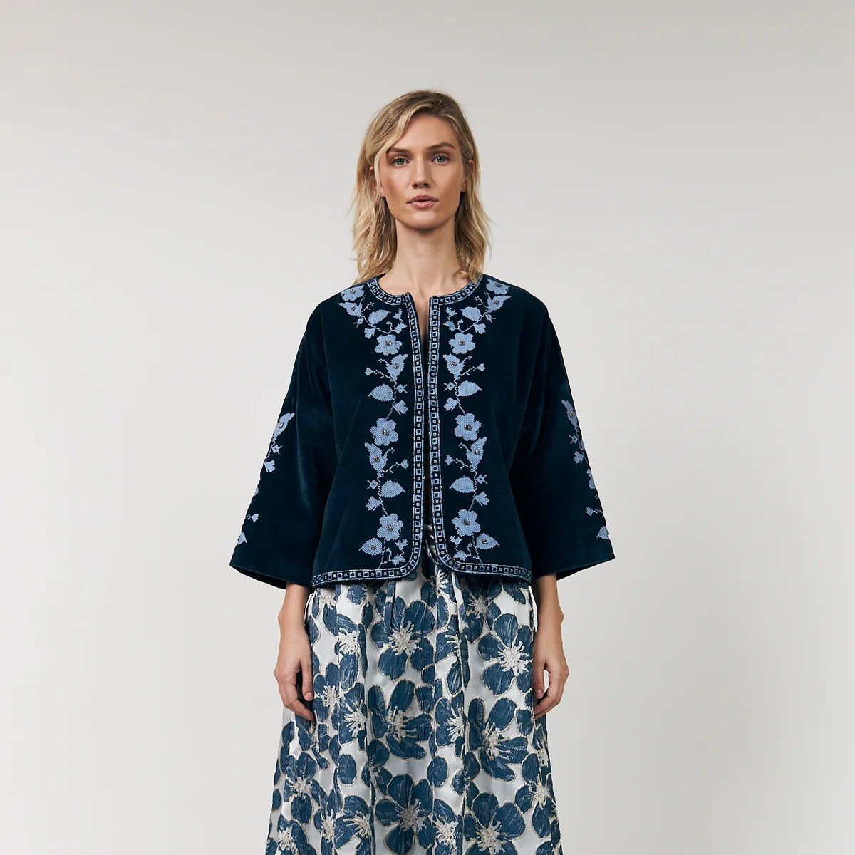 Woman wearing a dark blue embroidered top and floral skirt on a white background