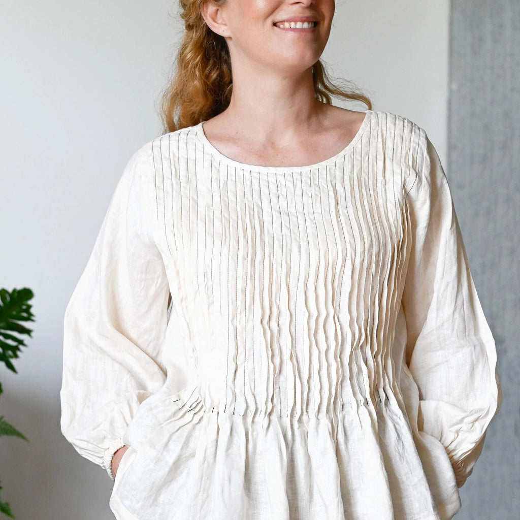 Woman wearing a white textured blouse with black pants against a neutral background