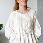 Woman wearing a white textured blouse with black pants against a neutral background
