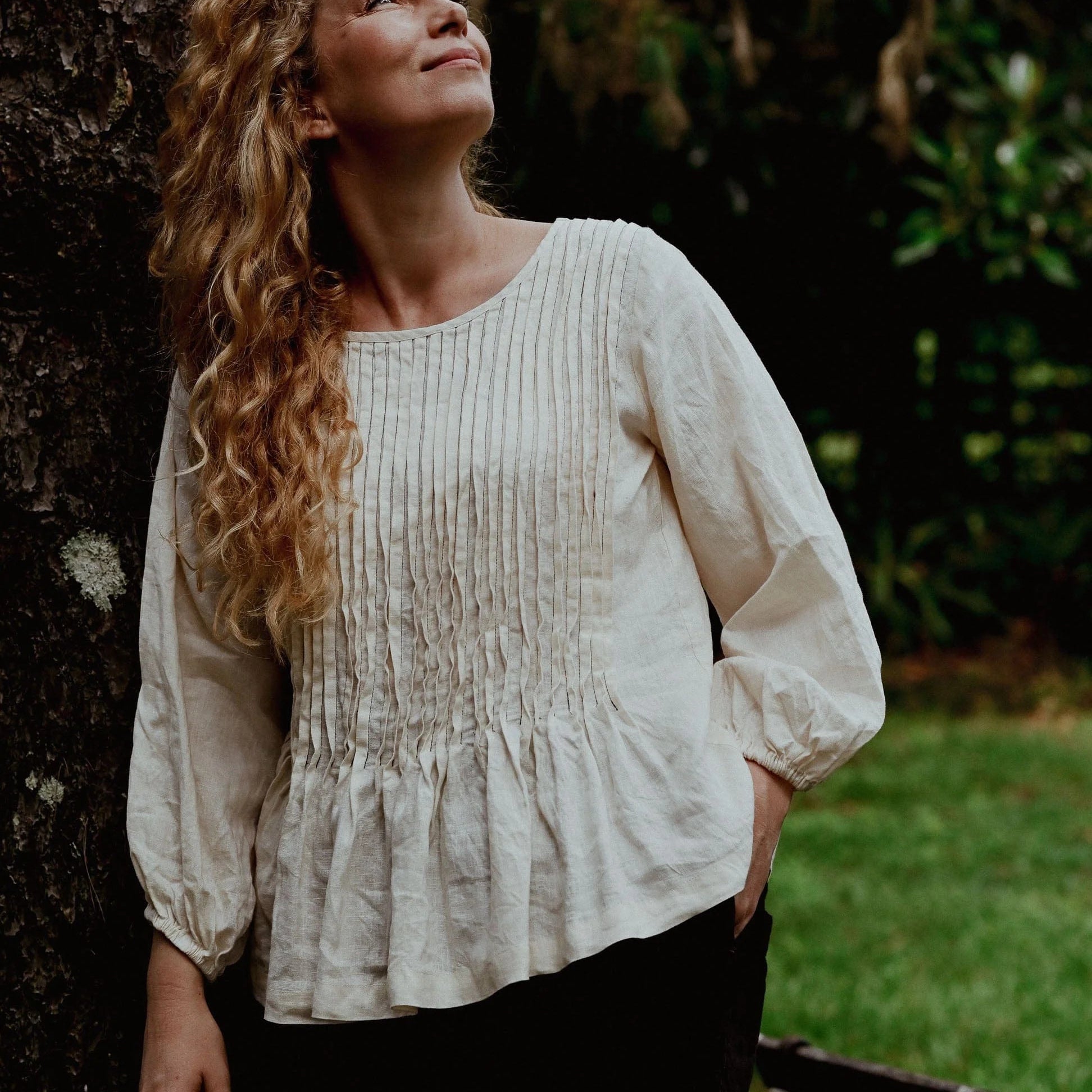 Woman in a white blouse standing next to a tree in a natural setting