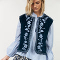 Woman wearing a blue embroidered vest over a light blue shirt with floral patterns on a white background