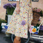 A person wearing a cream floral midi skirt and tan suede fringe ankle boots, standing outdoors near a bicycle and flower pots.