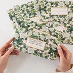 Set of floral-patterned stationery items held by hands on a white background