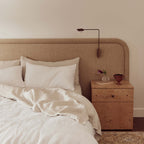 Neatly made bed with white bedding and pillows, nightstand with decorative items, and wall-mounted lamp.