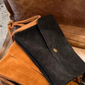 Black leather clutch on a brown leather surface
