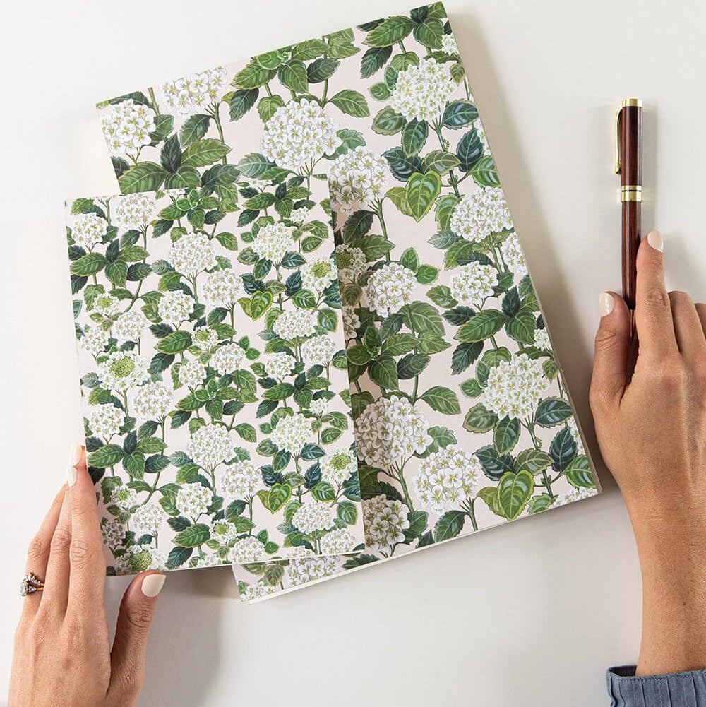 Person holding a floral-patterned notebook with a pen on a white background