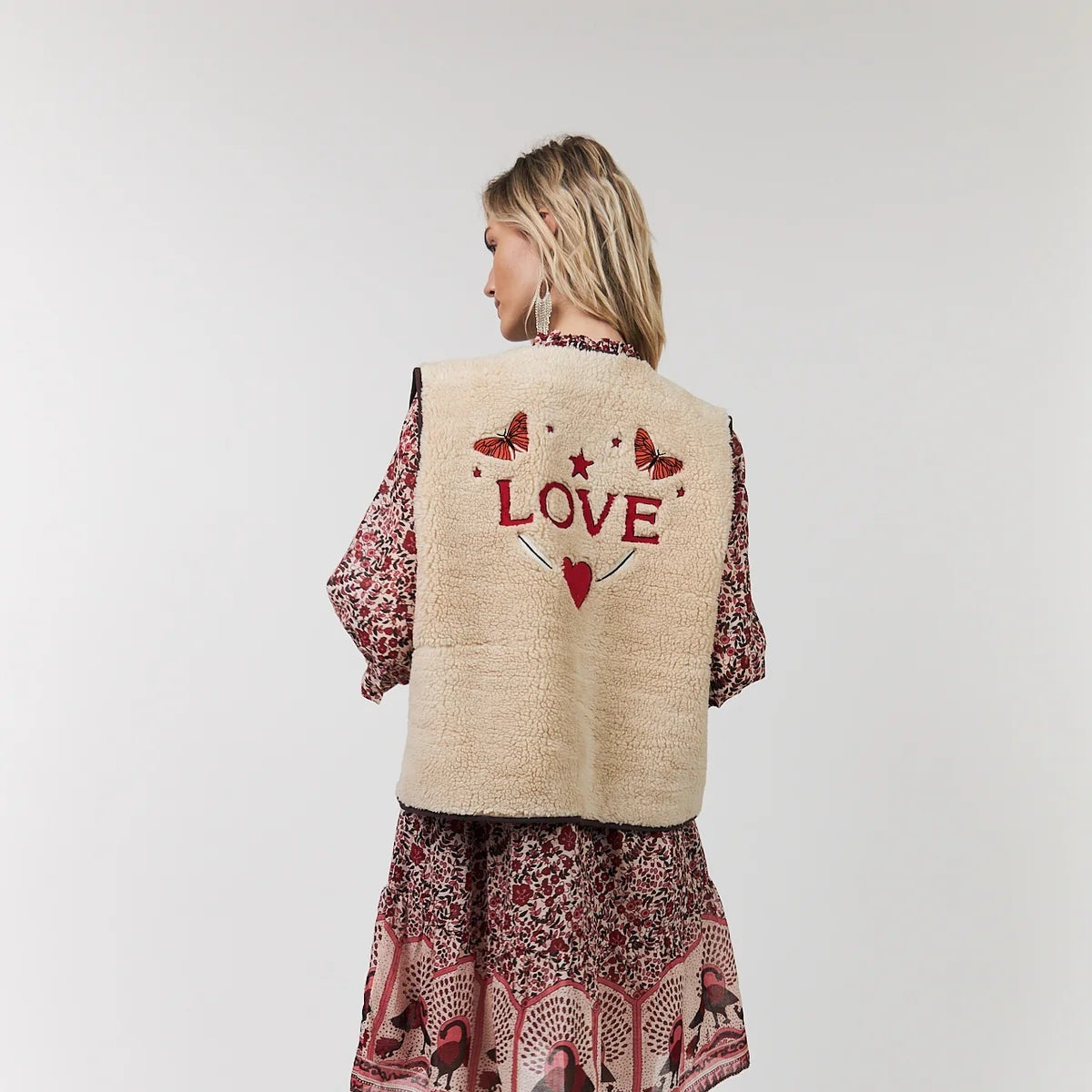 Woman wearing a patterned dress with 'LOVE' on a vest against a white background