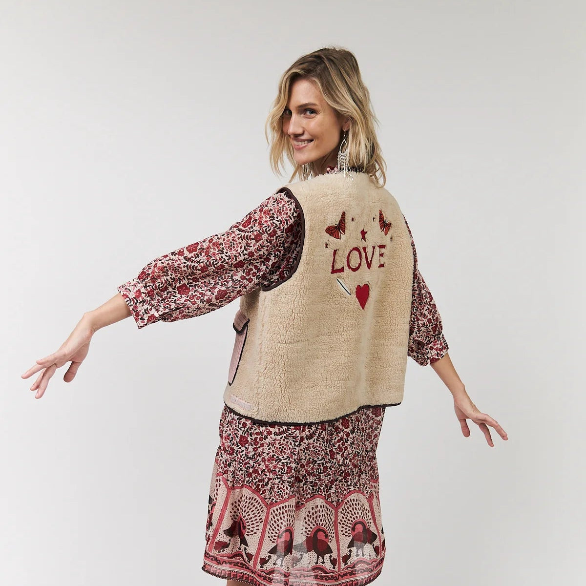 Woman wearing a patterned dress with a beige vest on a white background