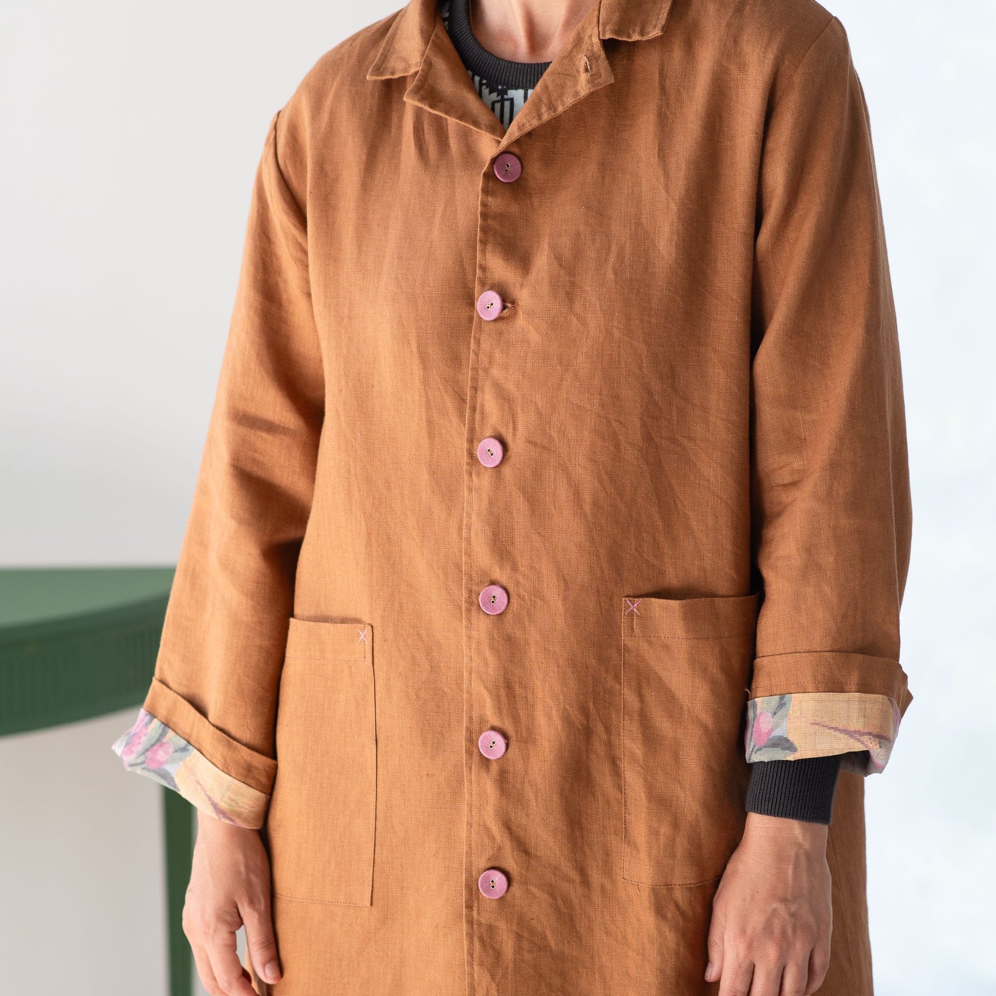 Person wearing a brown coat with pink buttons on a white background
