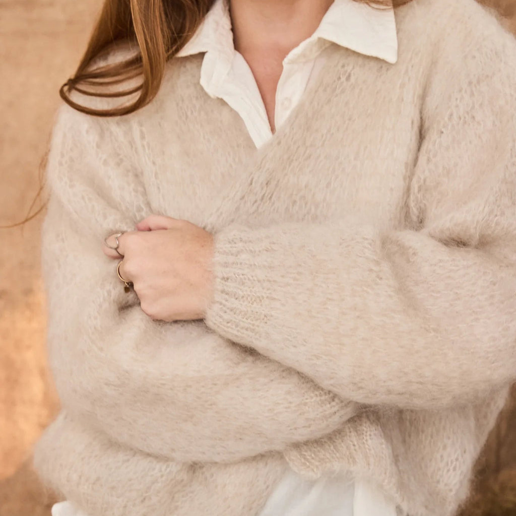 Person wearing a beige sweater over a white shirt with a blurred background