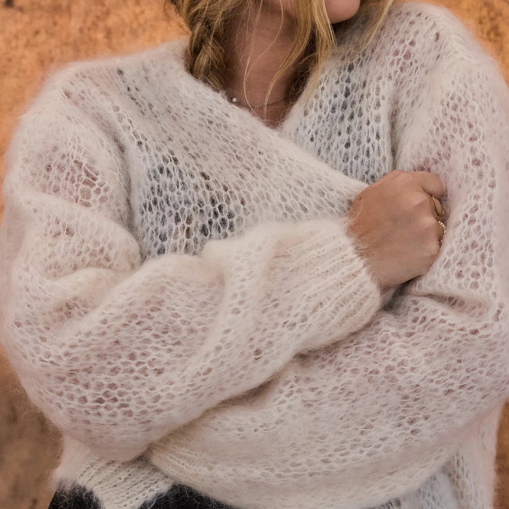 Woman wearing a light beige knitted sweater against a wooden background
