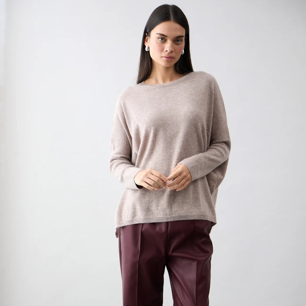 Woman wearing a beige sweater and burgundy pants against a white background