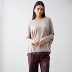 Woman wearing a beige sweater and burgundy pants against a white background