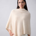 Woman wearing a beige poncho against a plain background