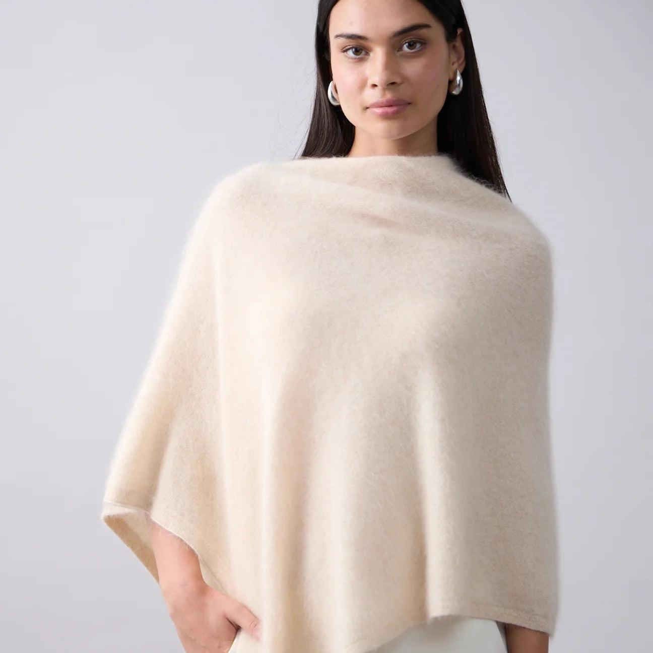 Woman wearing a beige poncho against a plain background