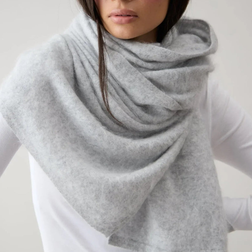 Person wearing a gray scarf over a white shirt and pants on a plain background