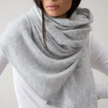 Person wearing a gray scarf over a white shirt and pants on a plain background