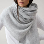 Person wearing a gray scarf over a white shirt and pants on a plain background