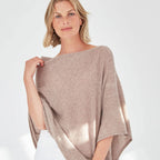 Woman wearing a beige poncho over a white outfit on a light gray background