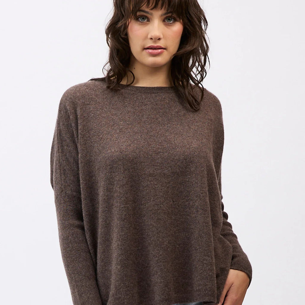 Woman wearing a brown sweater and light blue jeans on a white background
