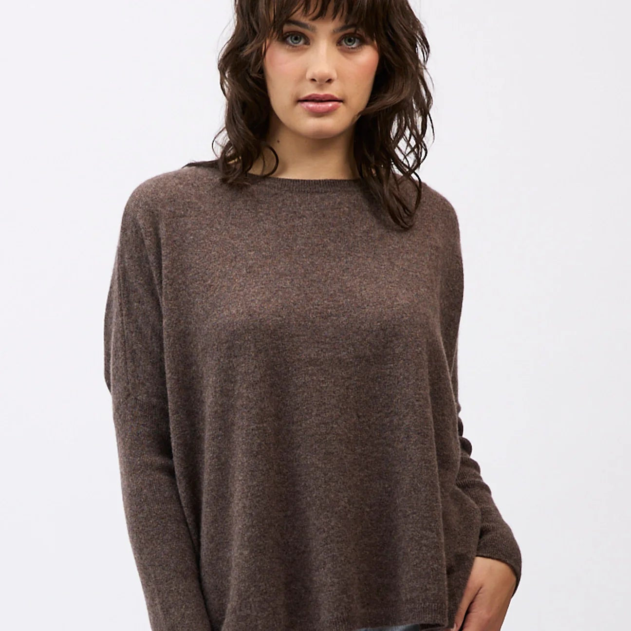 Woman wearing a brown sweater and light blue jeans on a white background