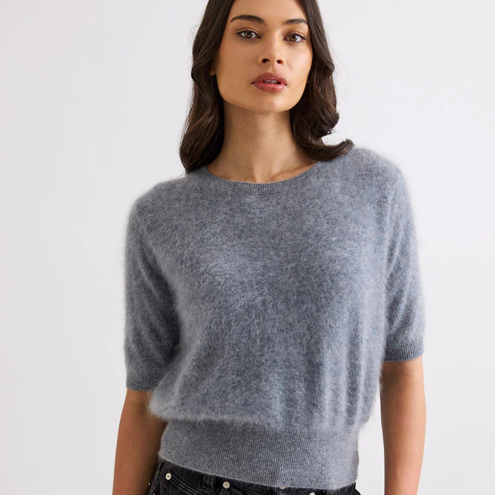 Woman wearing a gray sweater and black jeans against a white background
