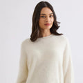 Woman wearing a cream sweater and blue jeans against a white background
