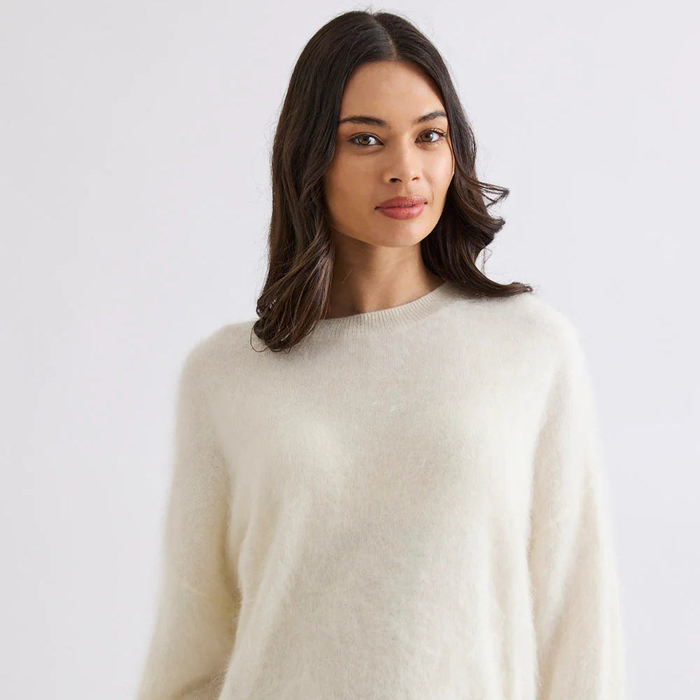 Woman wearing a cream sweater and blue jeans against a white background