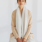 Woman wearing a beige cardigan and white scarf against a plain background