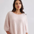 Woman wearing a light pink sweater and blue jeans on a white background