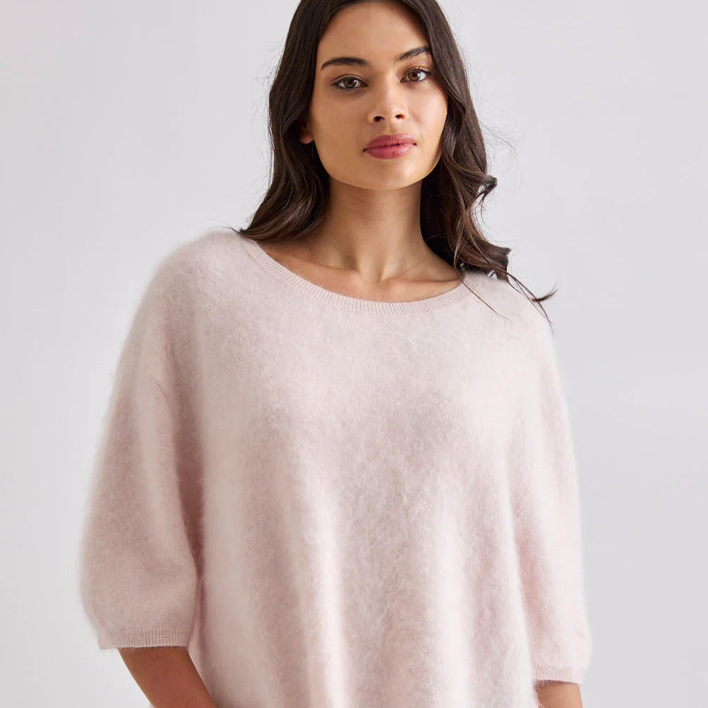 Woman wearing a light pink sweater and blue jeans on a white background