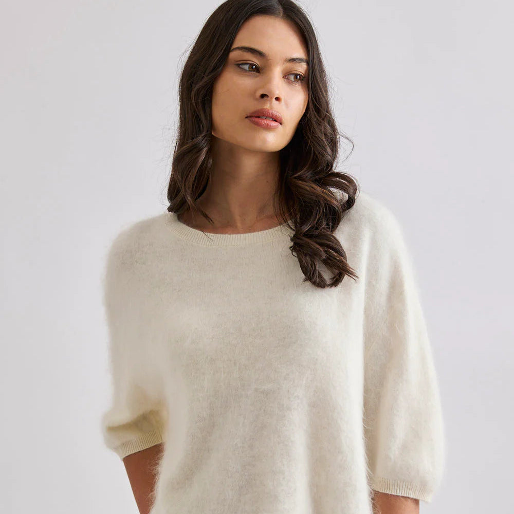 Woman wearing a beige sweater and blue jeans against a white background