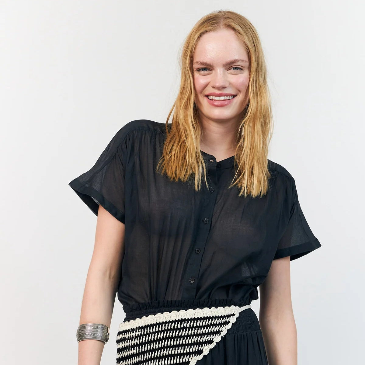 Woman wearing a black outfit with a white and black patterned belt against a white background