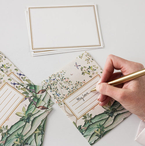 Hand writing on a floral card with other cards and stationery items on a light surface